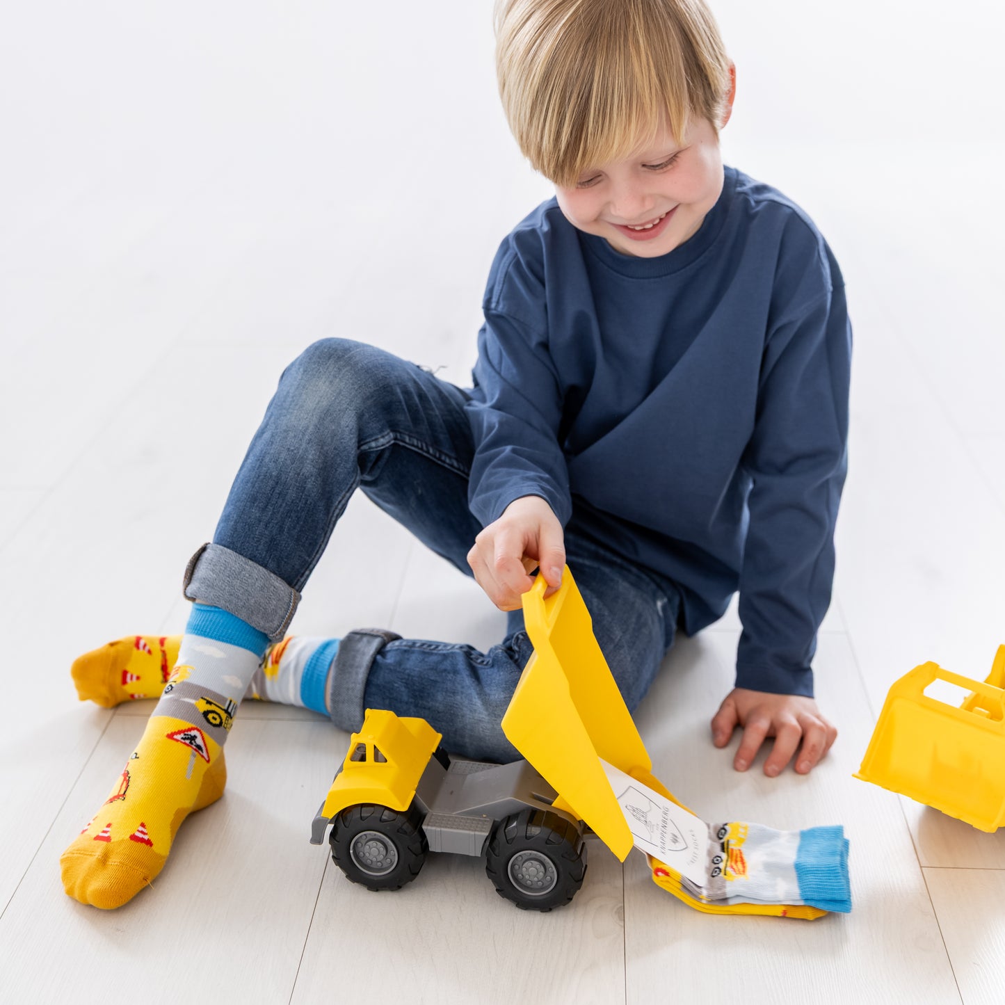 Ein Kind trägt die lustigen Baustellen-Socken beim Spielen mit seinem Spielzeug-Bagger.
