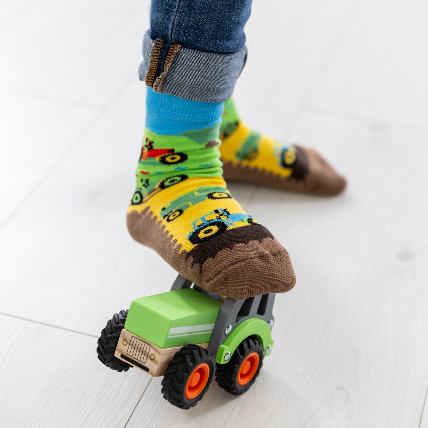 Ein Kind trägt die lustigen Traktor Socken beim Spielen mit Bauernhof-Spielzeug.