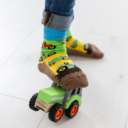 Ein Kind trägt die lustigen Traktor Socken beim Spielen mit Bauernhof-Spielzeug.
