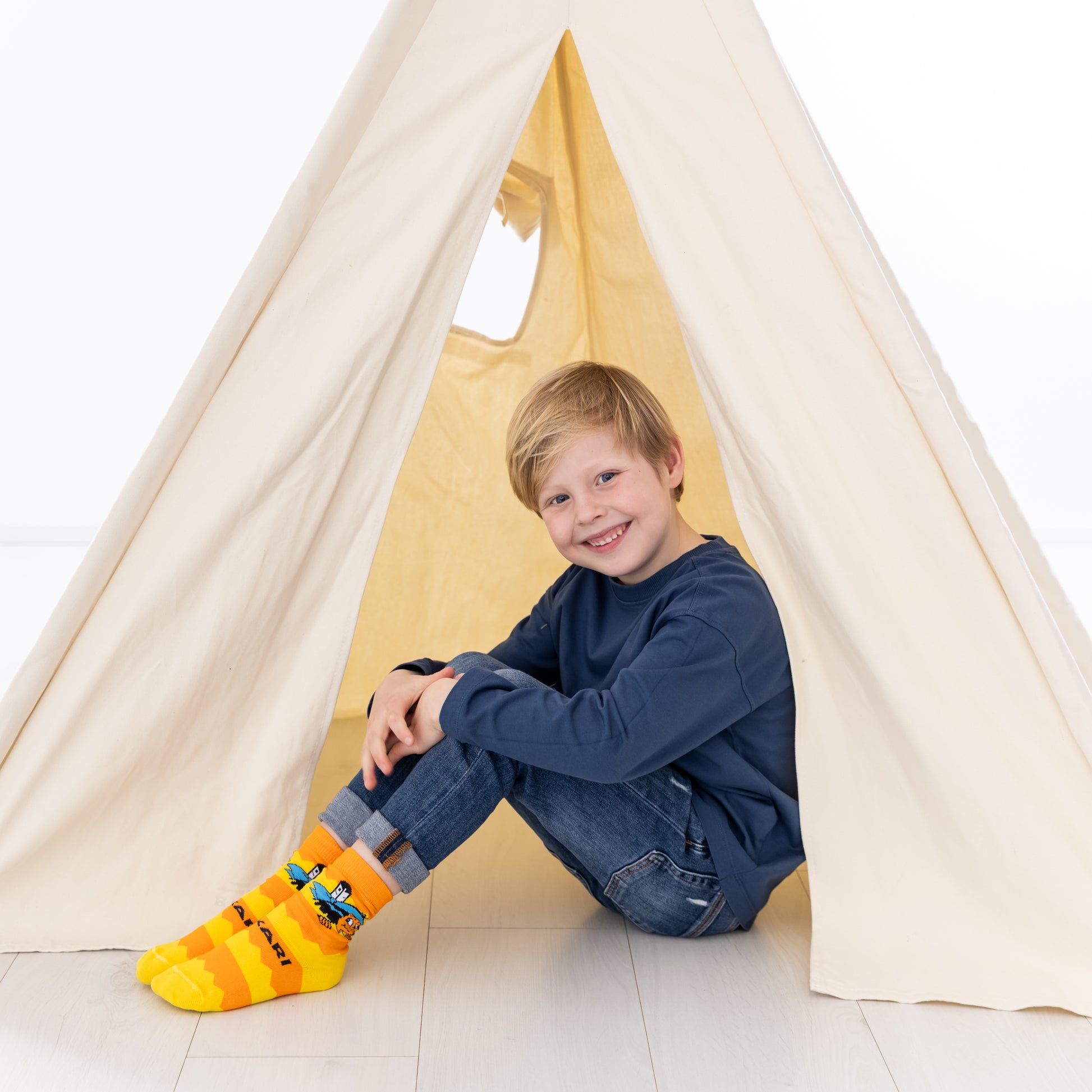 Ein Kind trägt die farbenfrohen Yakari Socken beim Spielen in einem Zelt.