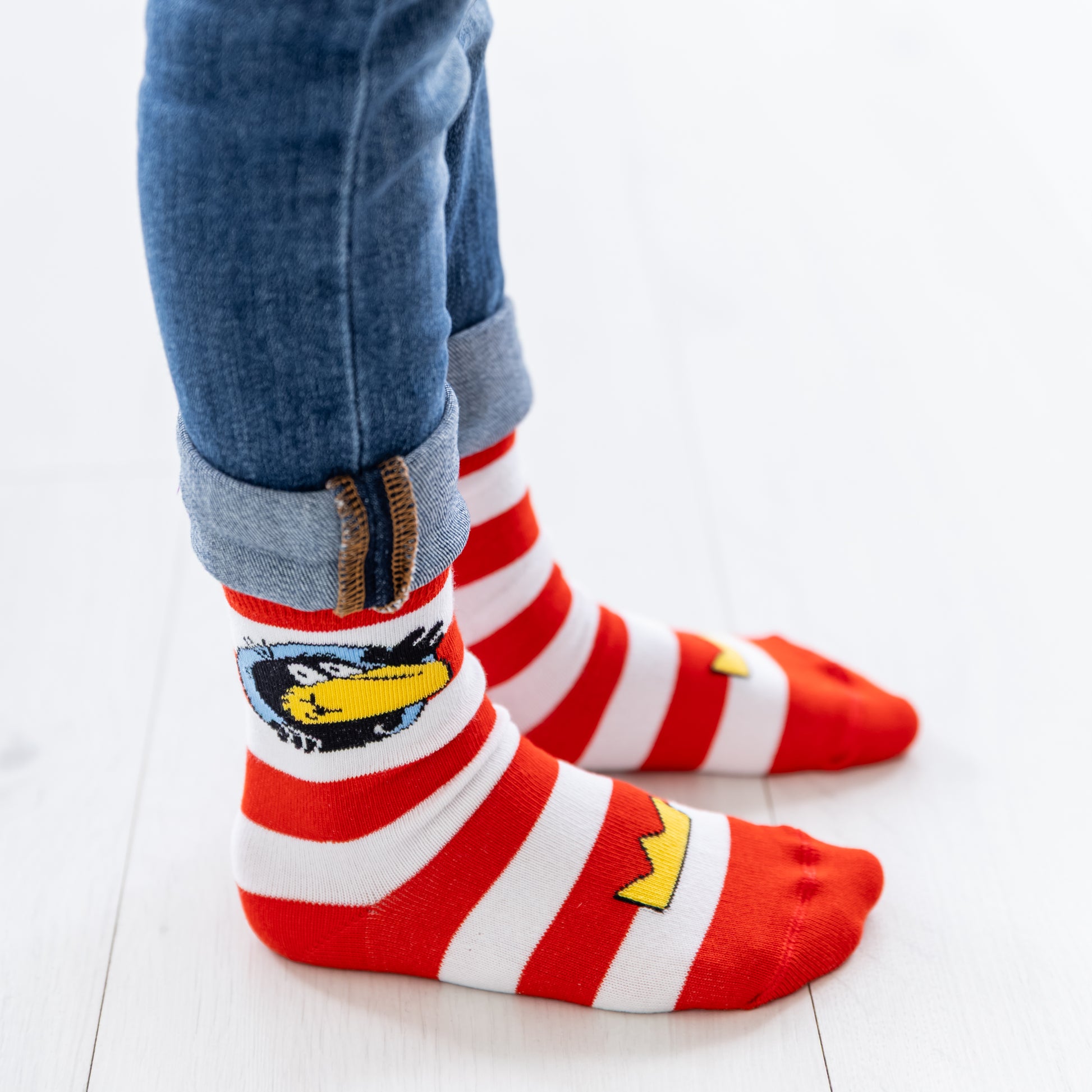 Ein Kind trägt die rot-weiß gestreiften Rabe Socke Socken an den Füßen.